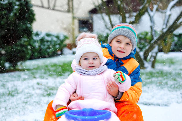 kleines kind junge und niedlichen kleinkind mädchen sitzen zusammen auf schlitten. geschwister, bruder und baby schwester schlittenfahrt bei schneefall zu genießen. kinder rodeln auf schnee. aktive unterhaltung für familienurlaub - little boys sled clothing slide stock-fotos und bilder