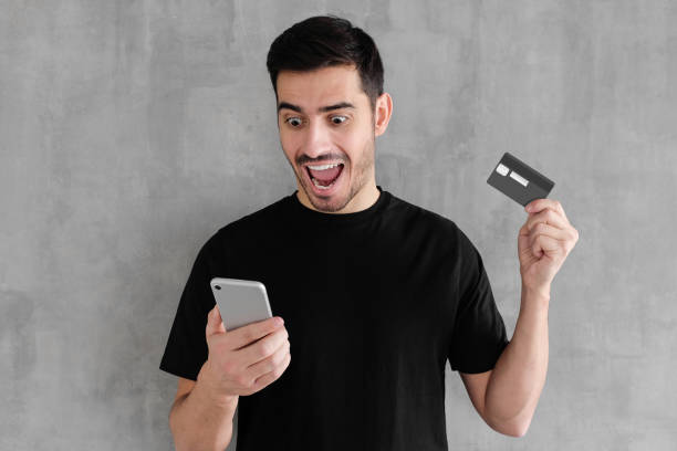 istock Young surprised handsome man holding credit card, using mobile phone with mouth open 1093999590