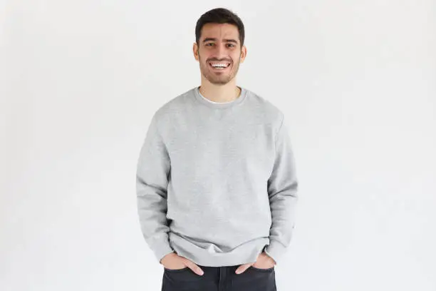 Daylight portrait of young laughing handsome man, wearing oversized sweatshirt, isolated on gray background