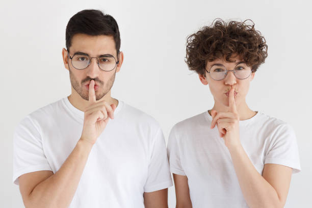 istock Young couple showing shh gesture isolated on gray background 1093999714