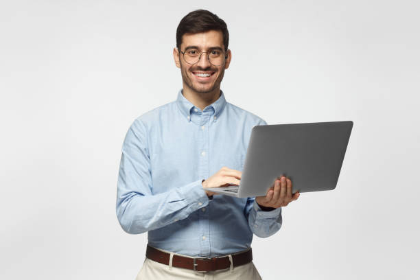 istock Handsome young man using laptop and looking at camera with smile, isolated on gray background 1093999956