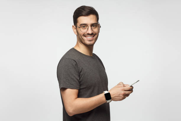 istock Young man standing isolated on gray background, holding smartphone, looking at camera and smiling nicely 1093999964
