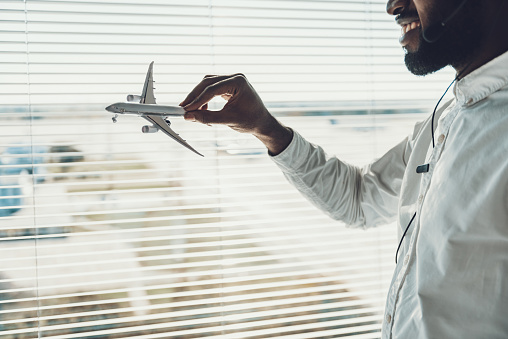 Center of dispatching maintenance. Close up side on portrait of smiling afro-american male specialist pretending to fly by airplane model in hand