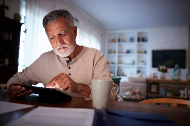 istock Senior Hispanic man sitting at his dining table reading an e book at home in the evening, close up 1094016150