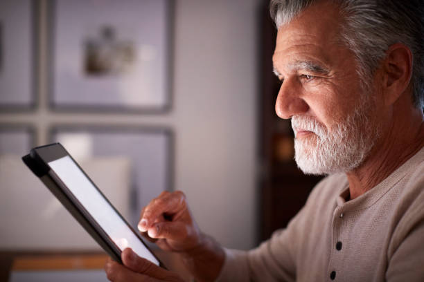 istock Senior Hispanic man sitting at a table using a tablet computer  in the evening, close up, side view 1094016160