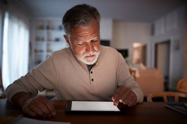 istock Senior Hispanic man sitting at a table using a tablet computer at home in the evening, close up 1094016178