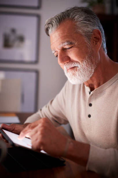senior-hispanic mann sitzt an einem tisch mit einem tablet-computer am abend hautnah, vertikale - senior adult digital tablet domestic life learning stock-fotos und bilder