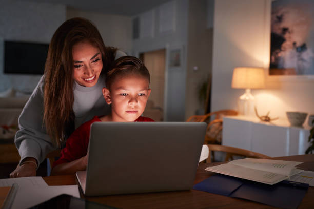 mujer hispana mirando sobre el hombro de sus hijos mientras realiza su tarea con el ordenador portátil - face to face twilight togetherness vertical fotografías e imágenes de stock
