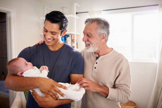 orgulloso padre hispano con su hijo de cuatro meses en casa, abuelo de pie al lado de ellos - abuelo y bebe fotografías e imágenes de stock