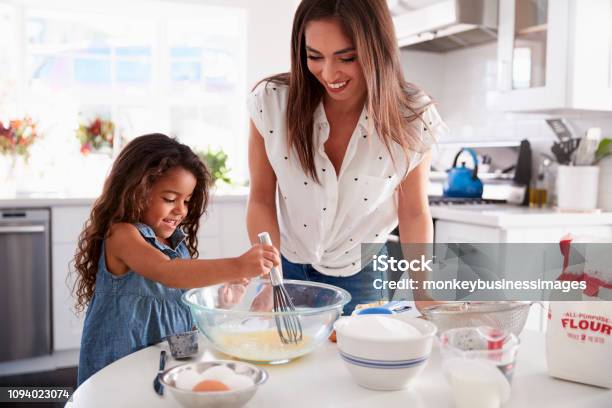 Young Hispanic Girl Making Cake In The Kitchen Overseen By Her Mum Waist Up Stock Photo - Download Image Now