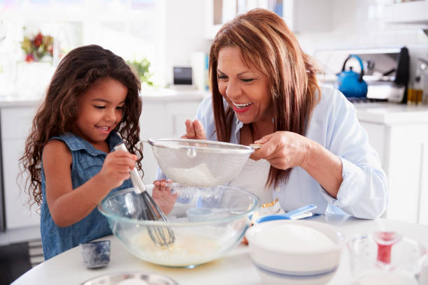 young hispanic girl making cake in the kitchen with her grandma, close up - grandmother cooking baking family imagens e fotografias de stock