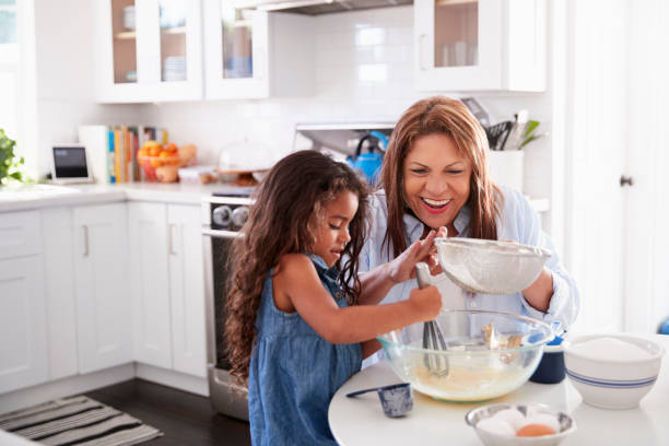 giovane ragazza ispanica che fa torta in cucina con sua nonna, guardando in basso - cake batter foto e immagini stock