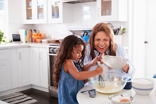 istock Young Hispanic girl making cake in the kitchen with her grandma, looking down 1094023390