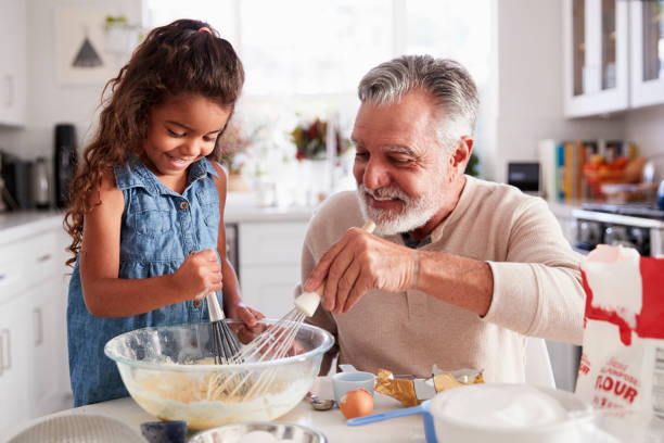 giovane ragazza ispanica e suo nonno che frusta miscela torta insieme al tavolo della cucina, da vicino - home baking foto e immagini stock