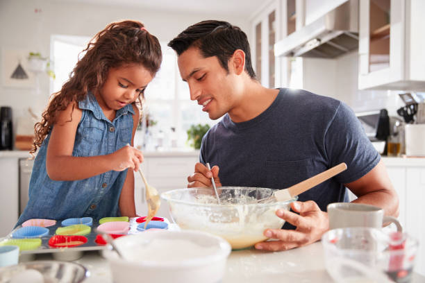 istock Young girl standing at the kitchen table making cakes with her father, filling cake forms, close up 1094025830