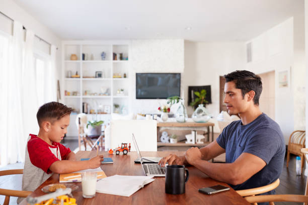 Hispanic father and son working opposite each other at the dining room table, side view, close up