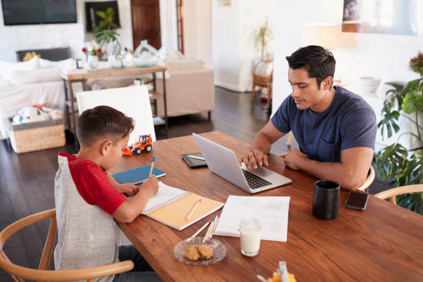 Hispanic father and son working opposite each other at the dining room table, elevated view Hispanic father and son working opposite each other at the dining room table, elevated view working at home with children stock pictures, royalty-free photos & images