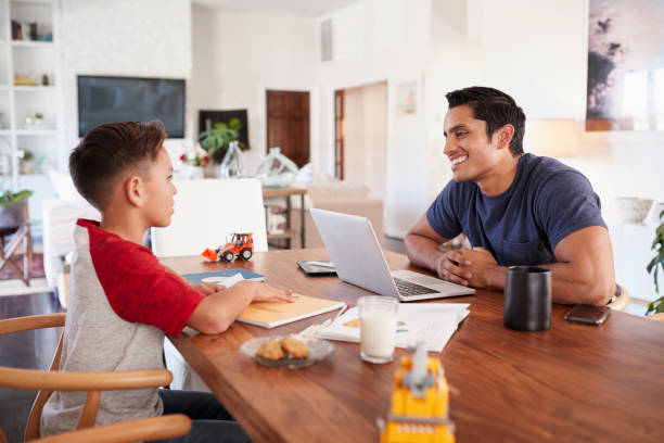 istock Hispanic father and son working opposite each other at the dining room table, selective focus 1094027028