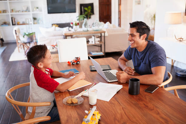 istock Hispanic father and son working opposite each other at the dining room table, side view 1094027272