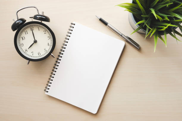 istock Empty white notebook top view with black alarm clock and pen on wooden table 1094027568