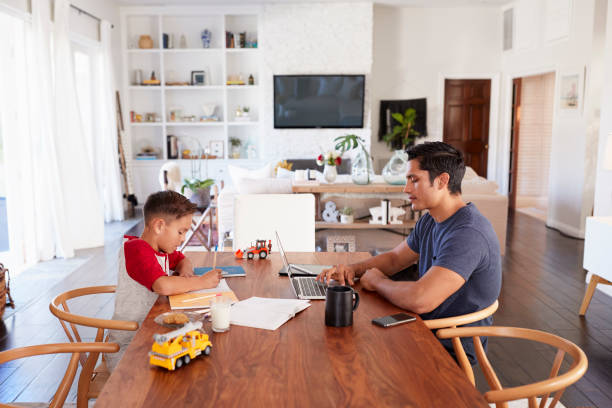istock Hispanic father and son working opposite each other at the dining room table, concentrating 1094027614
