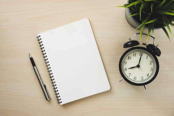 istock Empty white notebook top view with black alarm clock and pen on wooden table 1094027674