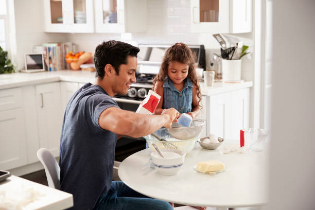 istock Young girl standing at the kitchen table preparing cake mixture with her father, seen from doorway 1094027922