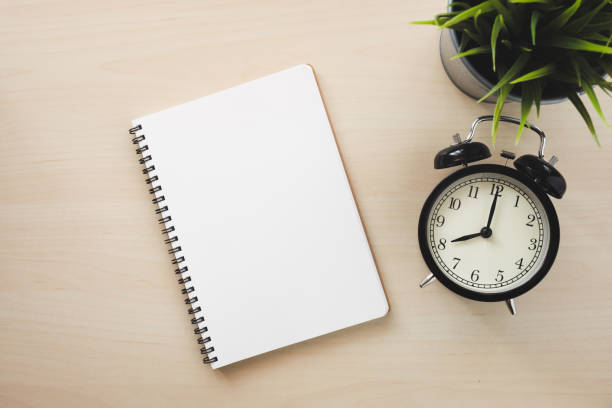 istock Empty white notebook top view with black alarm clock on wooden table 1094027940