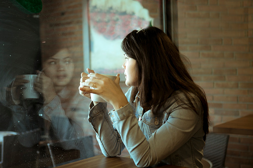 An Asian pretty woman drinking coffee  in indoor cafe of Jakarta city, Indonesia