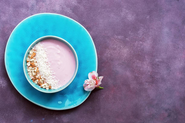 Fresh pink yogurt with nuts and coconut flakes in beautiful blue dishes on a purple background. Top view, place for test.