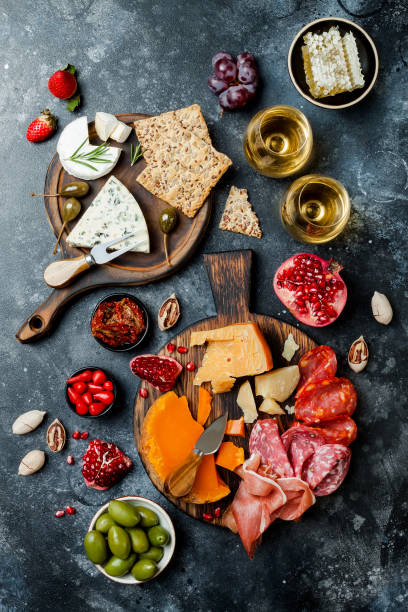 tavolo antipasti con snack antipasti italiani e vino in bicchieri. brushetta o autentico set di tapas tradizionali spagnole, tavola di varietà di formaggio su sfondo di pietra nera. vista dall'alto, lay piatto - wine cheese food salami foto e immagini stock