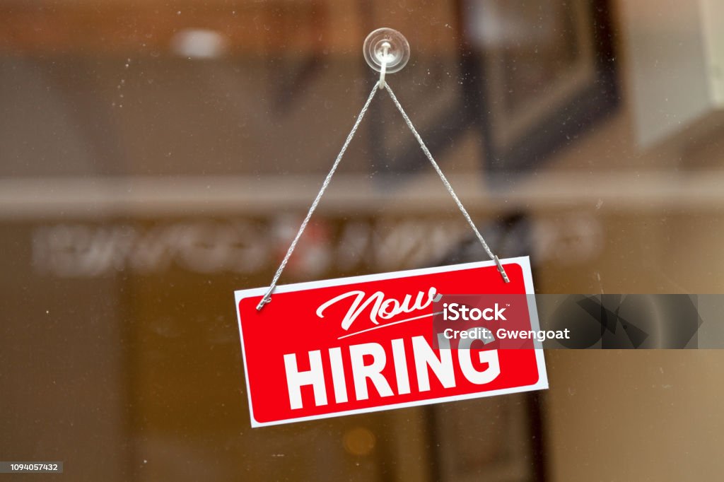 Now hiring sign Red sign hanging at the glass door of a shop saying: "Now hiring". Help Wanted Sign Stock Photo