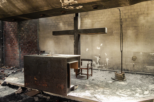 Beautiful altar and huge cross in a church or chapel destroyed by fire. Ruins of a recent burned religious place with natural lights. Power of fire.