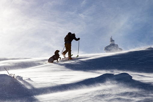 Back country skier hiking with his dog in the winter mountain in cold winter day.