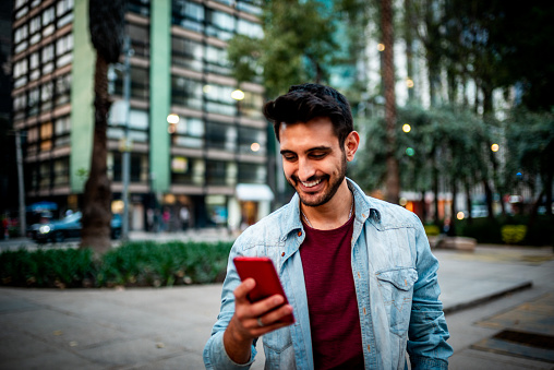 Portrait of a handsome smiling man using mobile phone at the street.