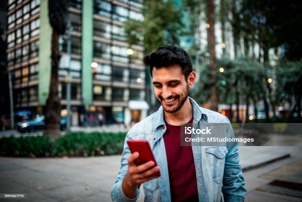 Handsome Indian man using mobile phone. Portrait of a handsome smiling man using mobile phone at the street. Men Stock Photo