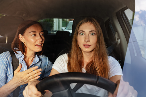 Portrait of surprised girl driving a car with her mother on the passenger seat