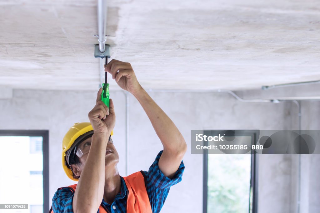 Electrician wiring on ceiling in construction site Electrician Stock Photo