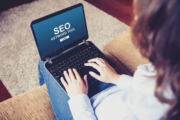 Woman using a laptop to do SEO positioning in a website while sitting on the sofa at home.