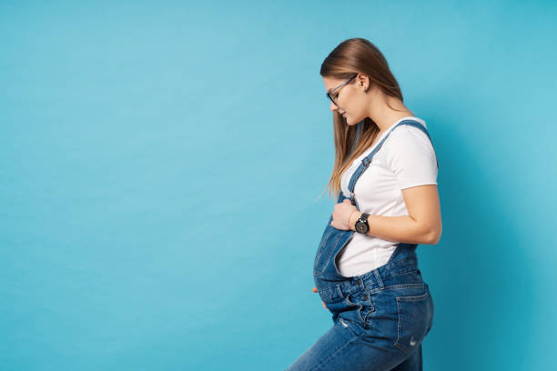 Smiling pregnant woman wearing glasses caressing her belly over blue background stock photo