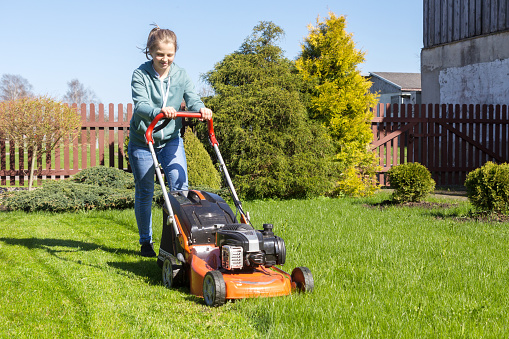teenage girl working in garden, mowing grass with lawn-mower