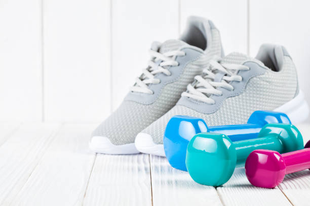 Sport and fitness symbols - sports shoes and colorful dumbbell on wooden wall background stock photo