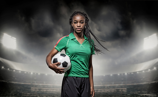 African Non-Caucasian Female Football Player Holding a Soccer Ball in front of Stadium Lights