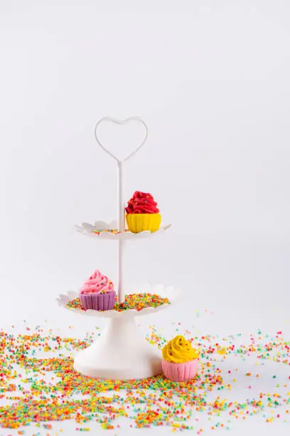 White two tier serving tray and miniature multicolored sugar cupcakes with sprinkles
