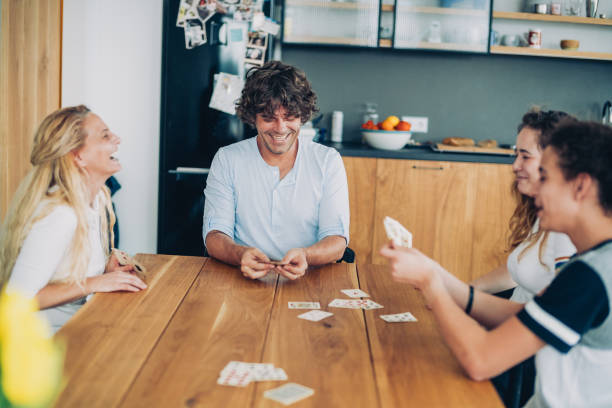 Cheerful Family Playing Cards Happy mother and father plays cards with their teenagers on the table at home family playing card game stock pictures, royalty-free photos & images