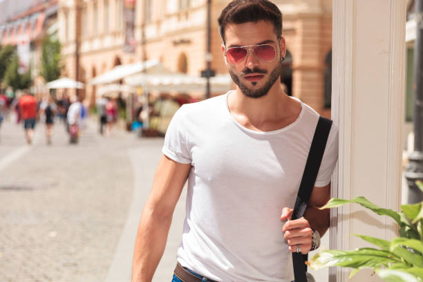 istock handsome young man holding shoulder bag and wearing sunglasses 1094128482
