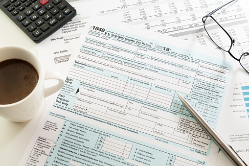 U.S. Individual Income Tax Return form 1040 with visible white cup of black coffee espresso, pen, calculator and eyeglasses on white table. Tax, accounting, business, finance and office concepts.