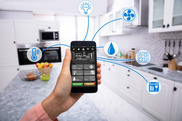 Woman's Hand Holding Mobile Phone Woman's Hand Using Home Control System On Cellphone With Various Icons In The Kitchen smart home technology stock pictures, royalty-free photos & images