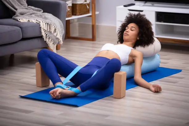 Relaxed Young Woman Lying On Fitness Mat Doing Exercise With Yoga Belt And Two Blocks