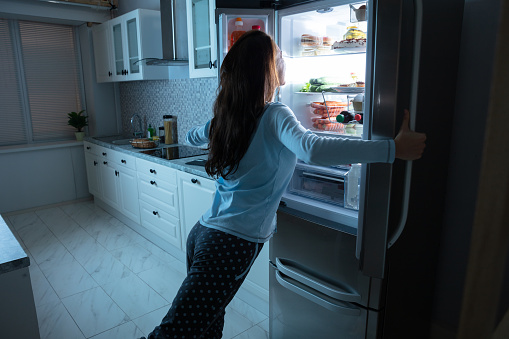 Woman Opening Refrigerator Door With Various Food In Kitchen